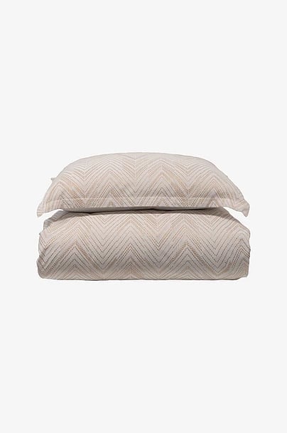 Folded beige chevron patterned bedding set with pillow and duvet on white background