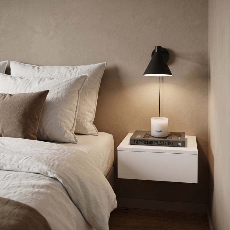 Minimalist bedroom corner with bed pillows, white nightstand, black table lamp, and stack of books