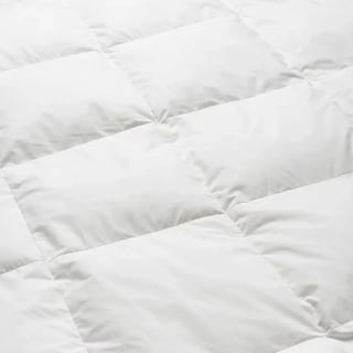 Close-up of white quilted duvet or comforter showing puffy quilted sections with stitched lines