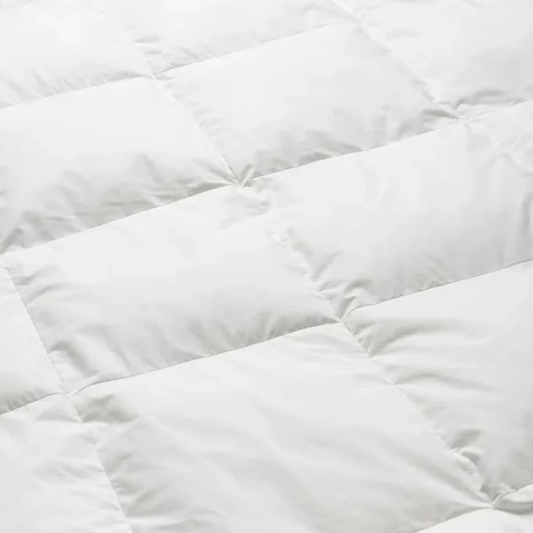 Close-up of white quilted duvet or comforter showing puffy quilted sections with stitched lines