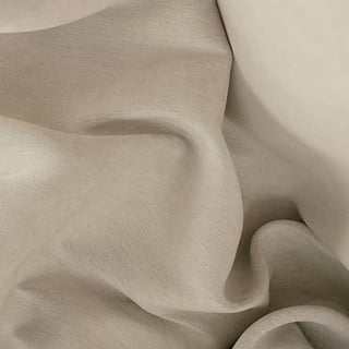 Close-up of soft, beige fabric with flowing folds and gentle shadows showing texture and drape