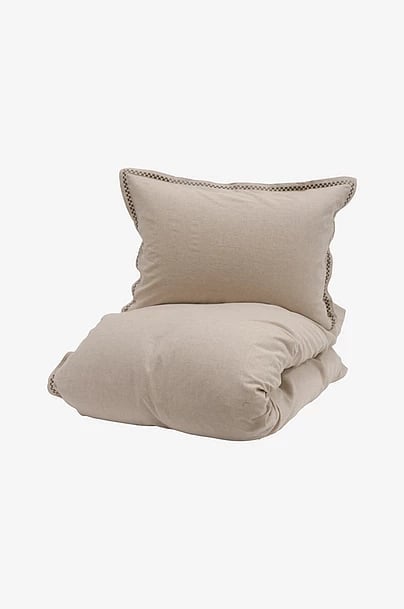 Beige linen pillows and duvet stacked together on white background, showing textured fabric with decorative stitching