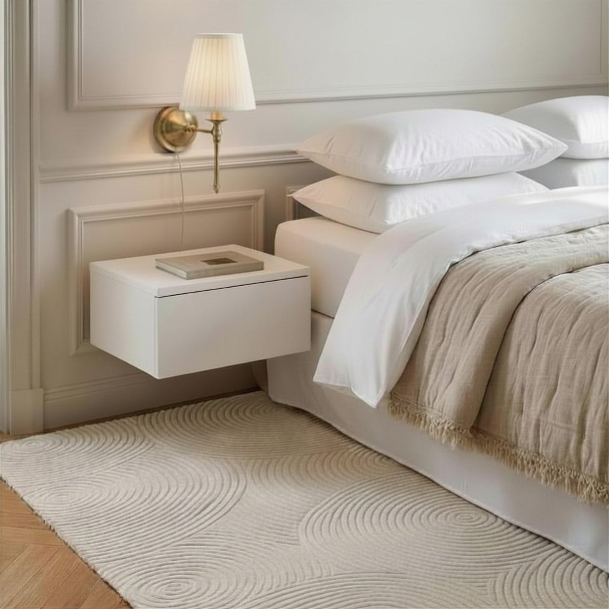 Modern bedroom with white nightstand, brass wall sconce, white pillows, beige bedding, and geometric patterned area rug
