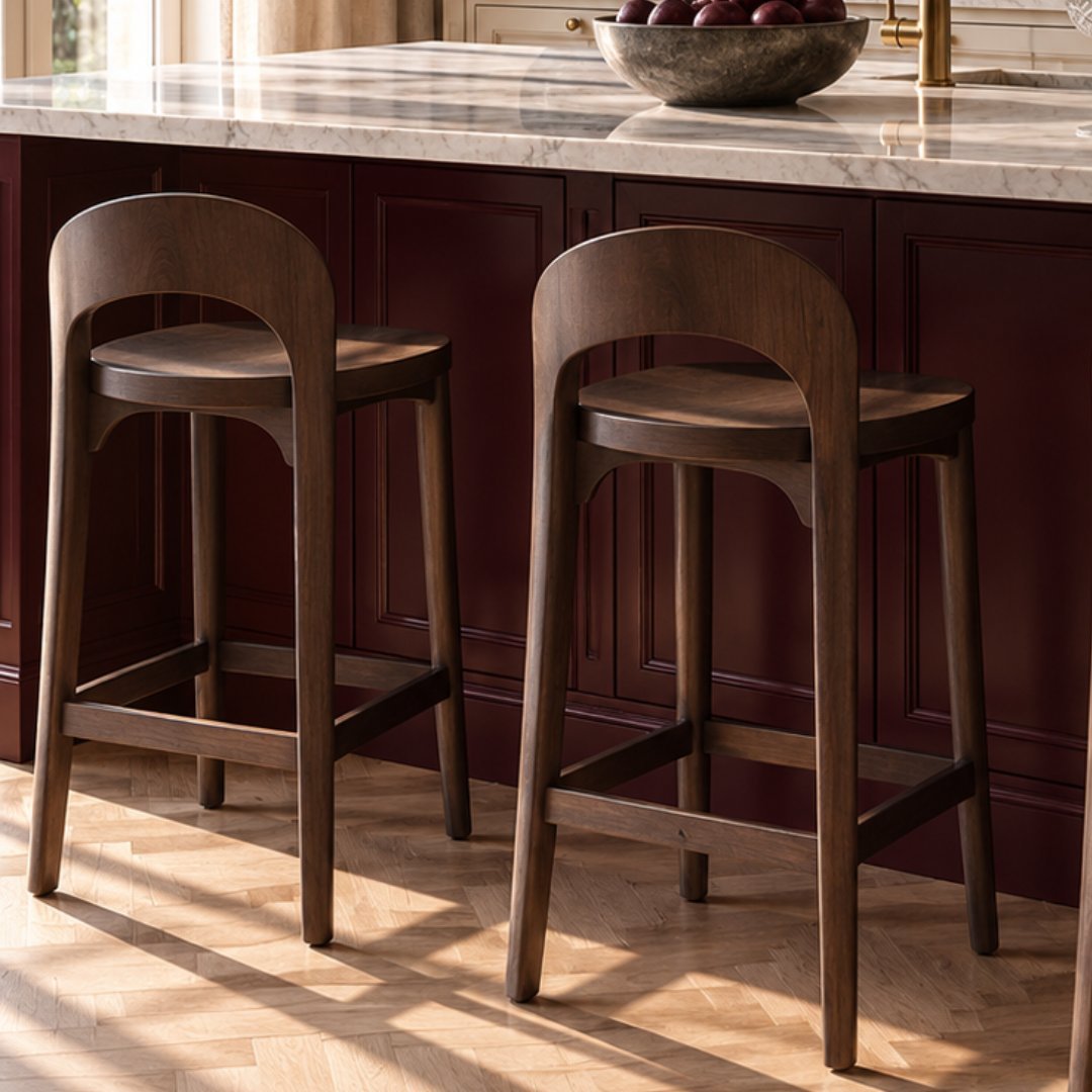 Two wooden bar stools with curved backs and leather seats positioned at a dark kitchen island with a marble countertop