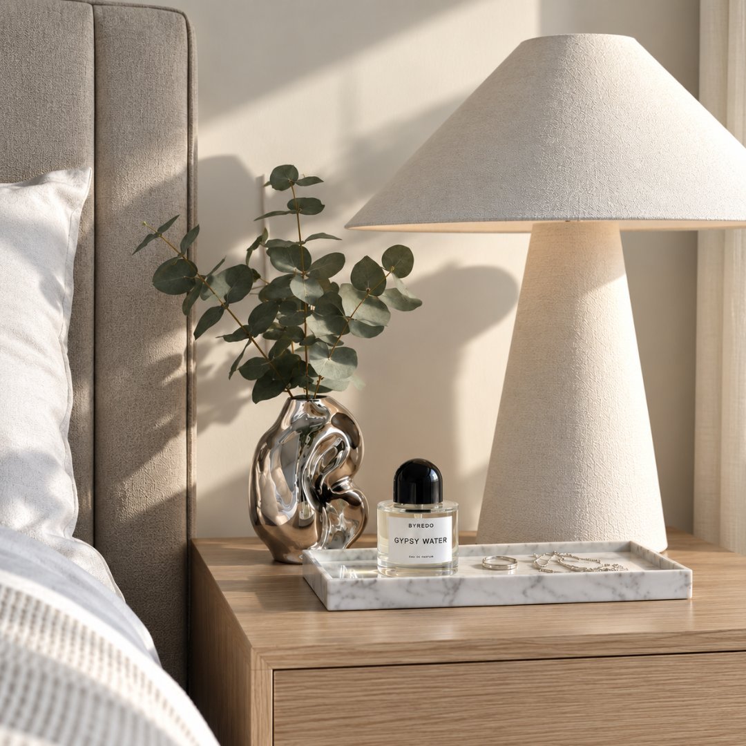 Minimalist bedside table with ceramic lamp, eucalyptus branch in glass vase, and perfume bottle on wooden nightstand